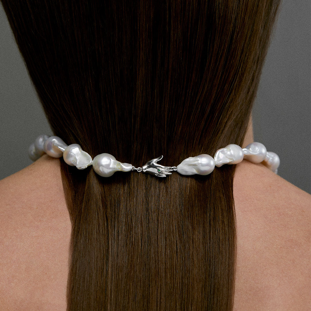 Model wearing baroque pearl necklace with sterling silver hand clasp and emerald