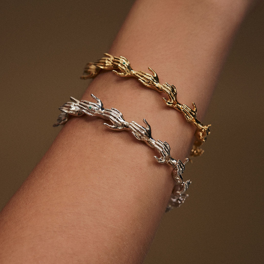 Model wearing hand-shaped bracelets in sterling silver chain with 18k gold plating and emeralds