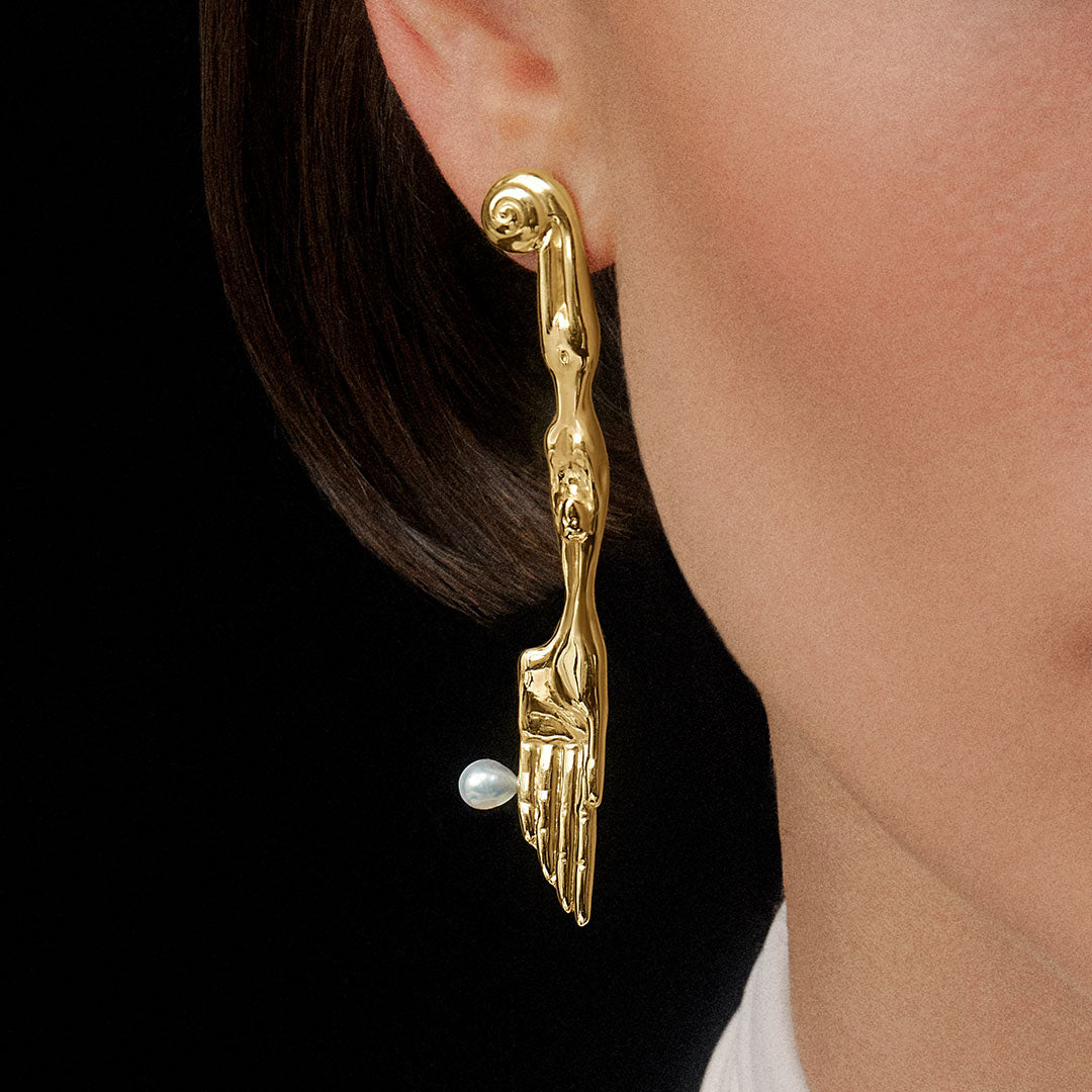 Model wearing sterling silver earring with 18k gold plating in the shape of a knife with surrealist body and natural pearl