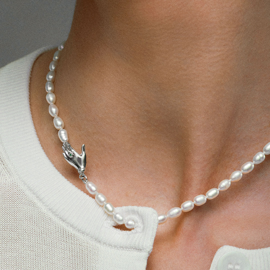 Model wearing pearl necklace with hand-shaped clasp in sterling silver adorned with emerald