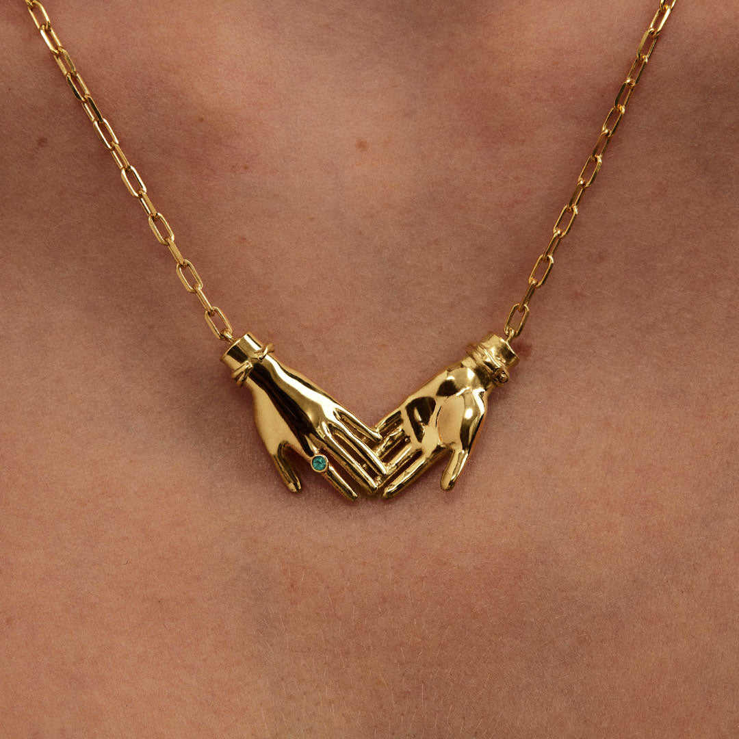 Model wearing sterling silver necklace with 18k gold plating featuring joined hands adorned with emerald
