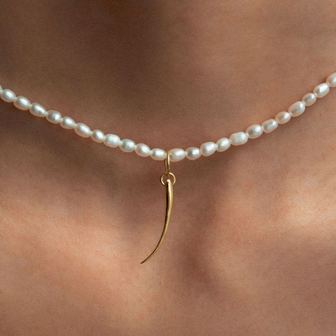 Model wearing 18k gold eyelash pendant on a pearl necklace