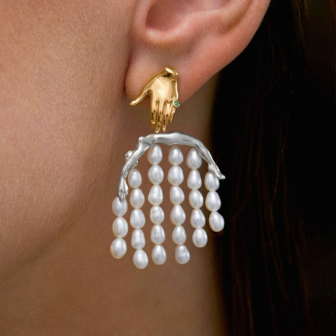 Model wearing 18k gold-plated sterling silver earring featuring a hand and body adorned with pearls and emerald
