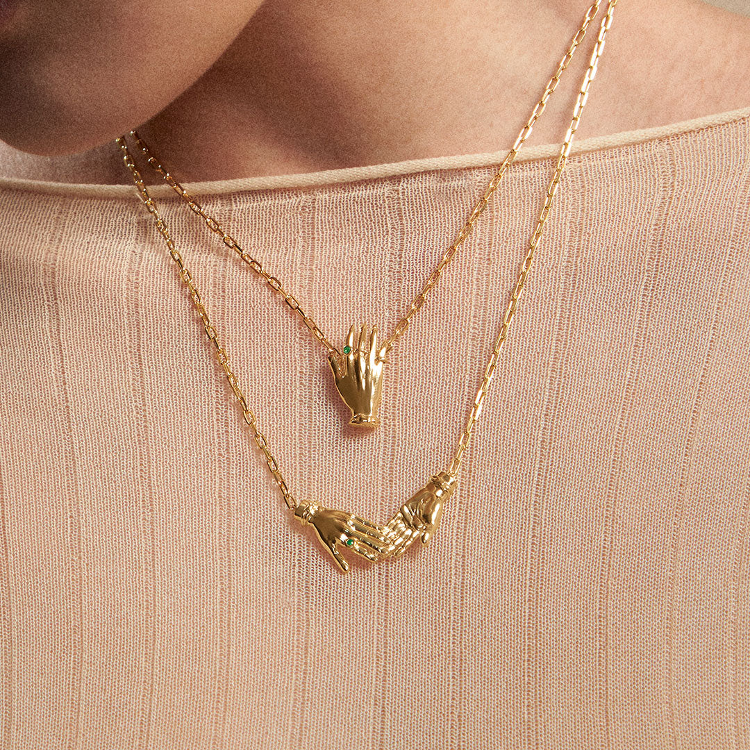 Model wearing necklaces in sterling silver with 18k gold plating featuring hands adorned with emeralds