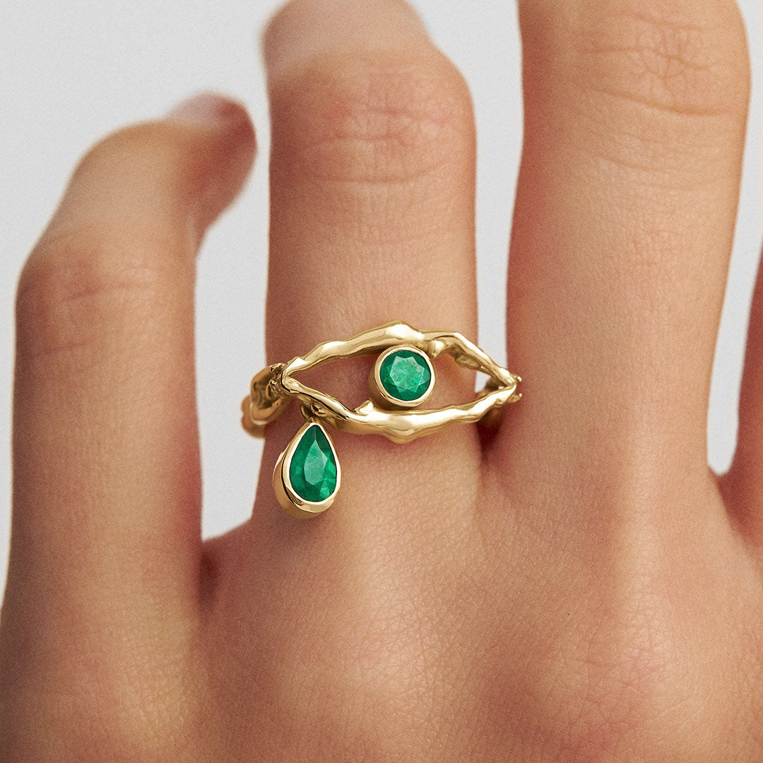 Model wearing 18k gold ring of bodies in eye shape adorned with emeralds