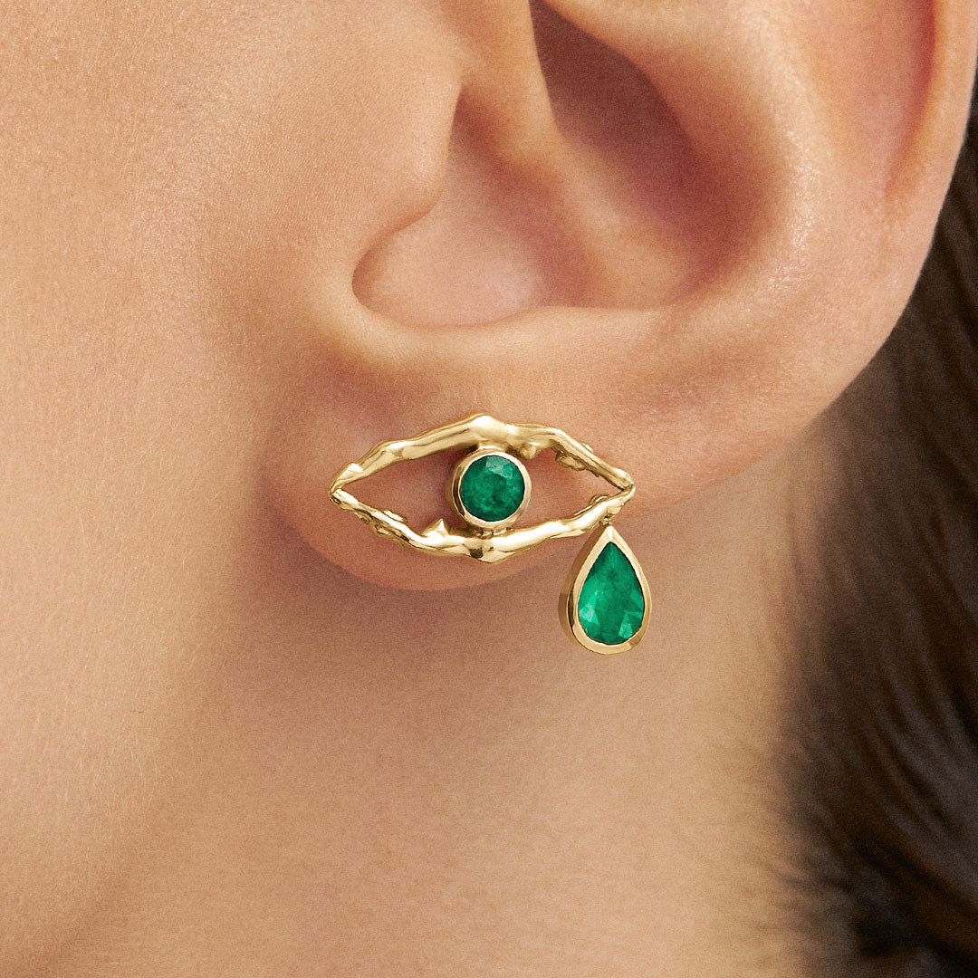 Model wearing 18k gold earrings with feminine bodies and emeralds