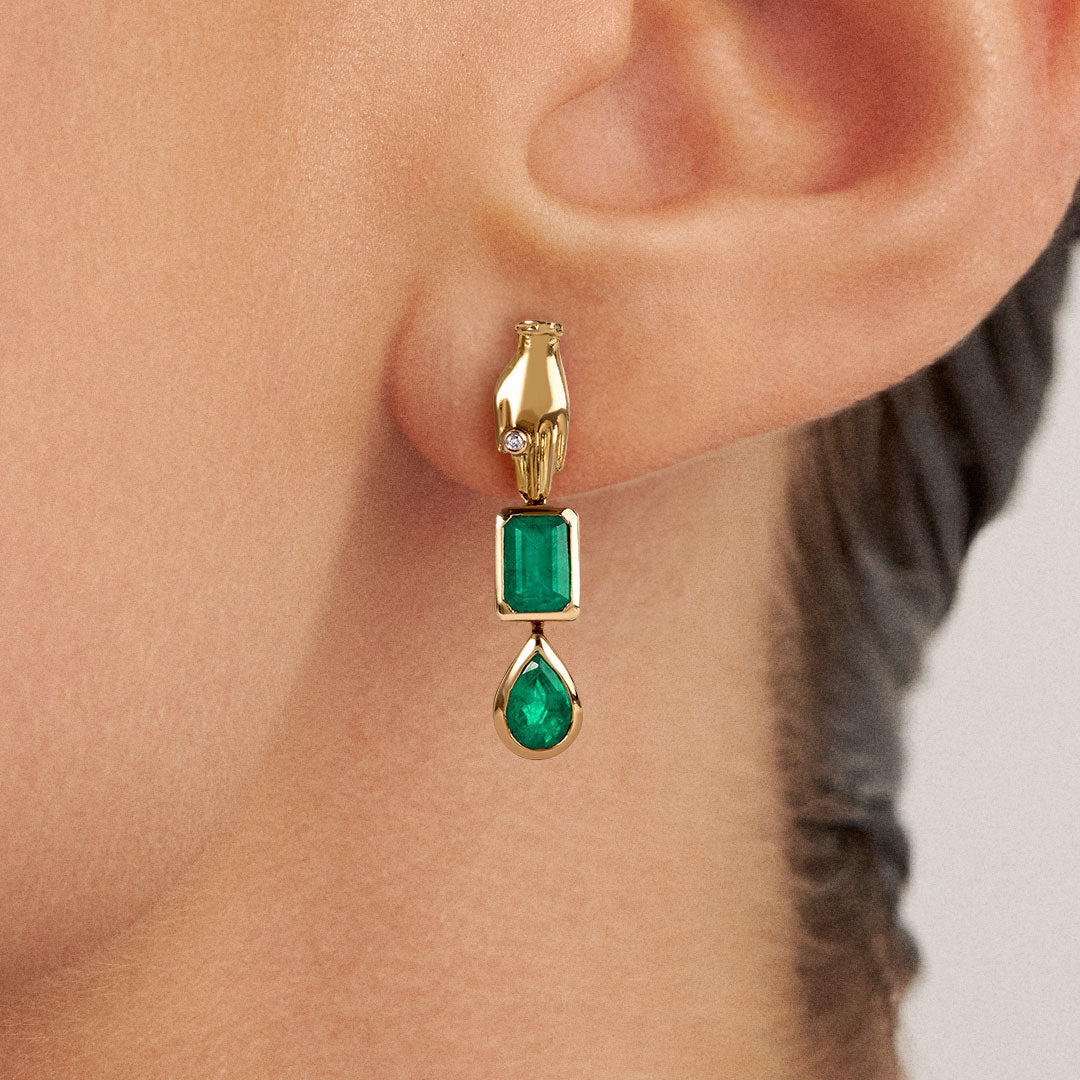 Model wearing 18k gold hand earring adorned with emeralds and a diamond