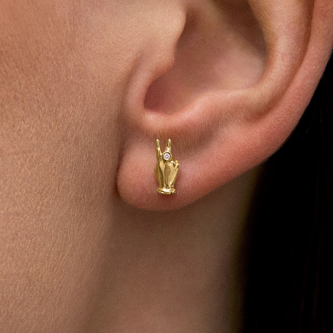 Model wearing 18k gold earring of a mini hand in a peace sign with diamond