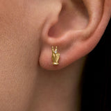 Model wearing 18k gold earring of a mini hand in a peace sign with diamond