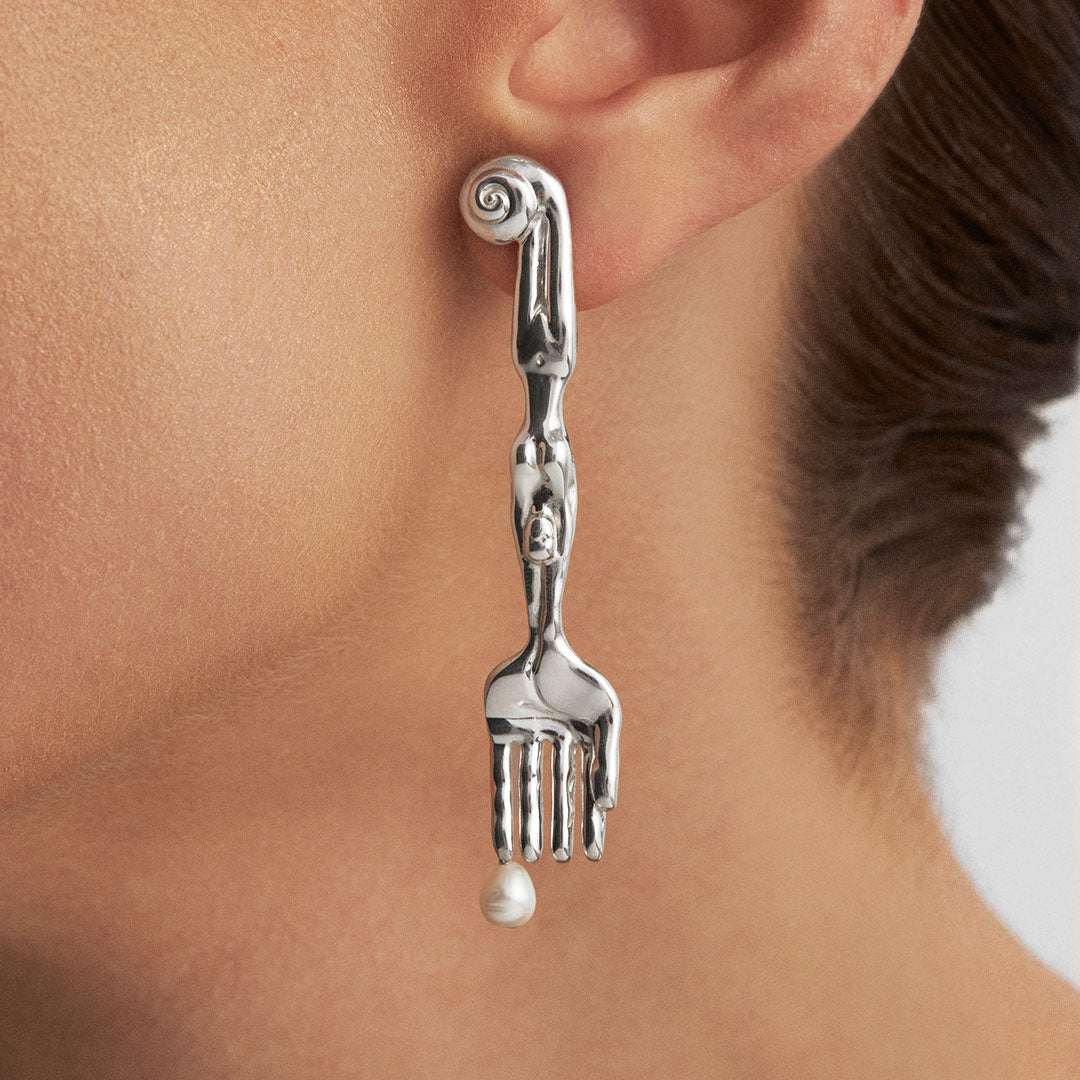 Model wearing sterling silver earring in the shape of a fork with surrealist body and natural pearl