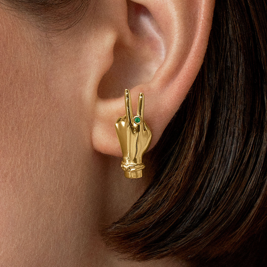 Model wearing hand-shaped earrings with peace sign in 18k gold-plated sterling silver and emerald