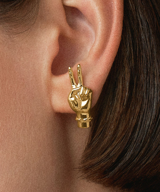 Model wearing hand-shaped earrings with peace sign in 18k gold-plated sterling silver