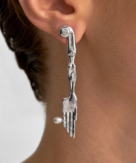 Model wearing sterling silver earring in the shape of a knife with surrealist body and natural pearl