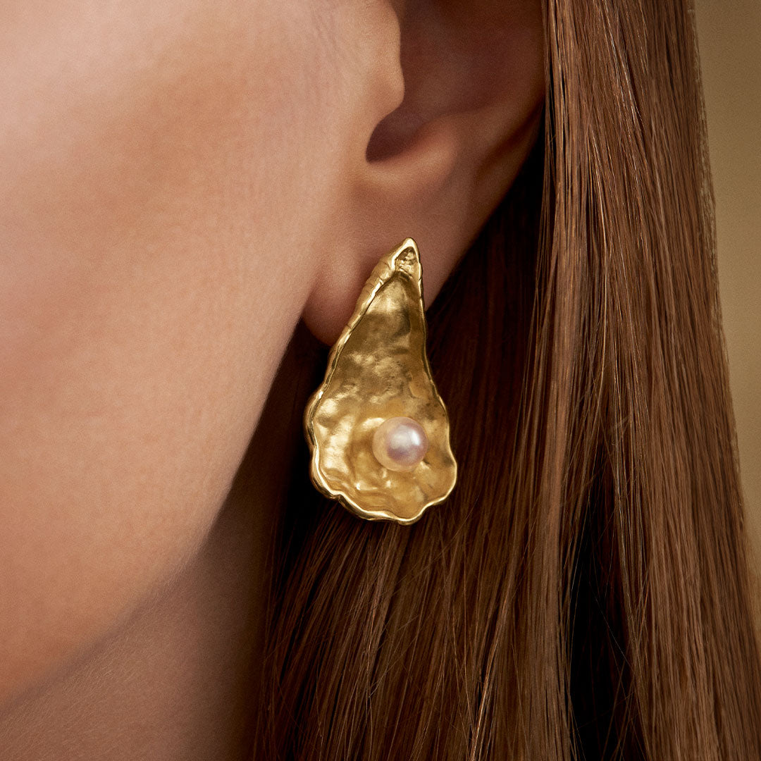 Model wearing large oyster earring in sterling silver with 18k gold plating and pearl