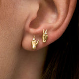 Model wearing 18k gold earrings of mini hands in peace and middle finger gestures with diamonds