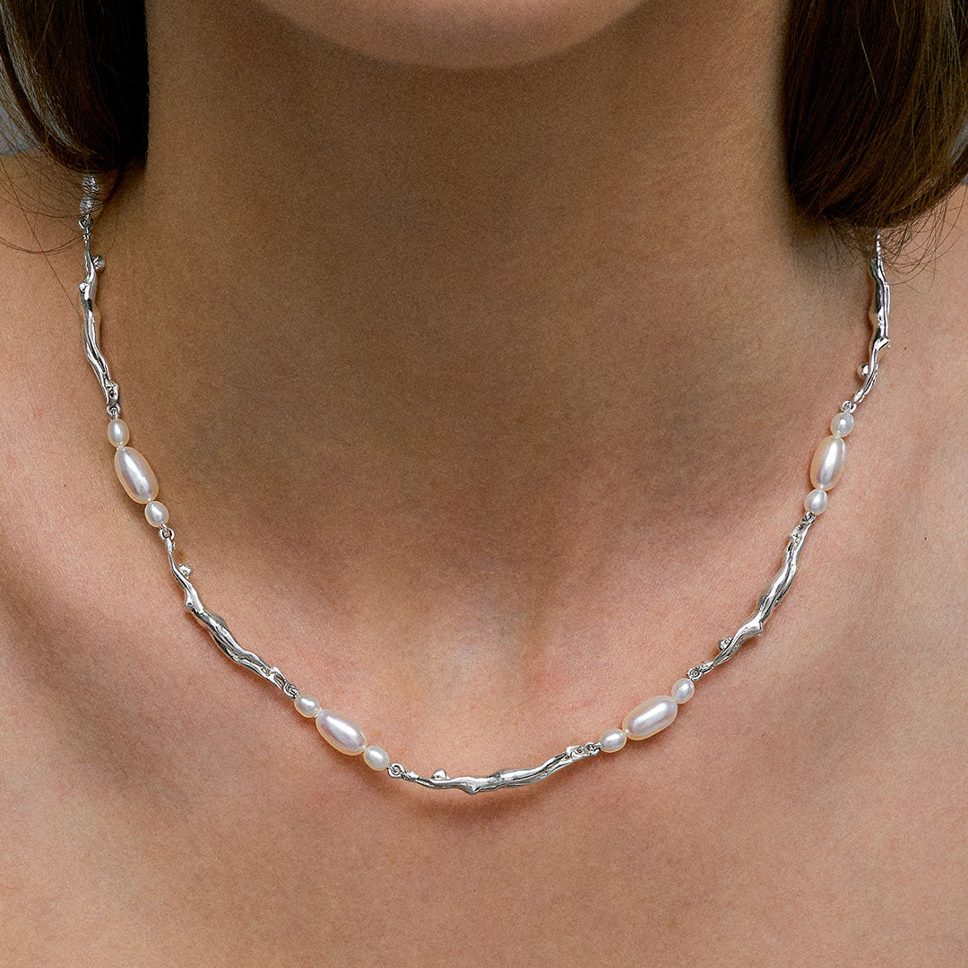 Model wearing necklace of feminine bodies in sterling silver and pearls adorned with emerald