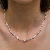 Model wearing necklace of feminine bodies in sterling silver and pearls adorned with emerald
