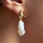 Model wearing hand-shaped earring in sterling silver with 18k gold plating, emerald, and baroque pearl