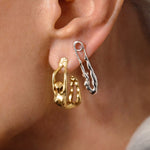 Model wearing sterling silver earrings with 18k gold plating featuring hoop and safety pin with female bodies