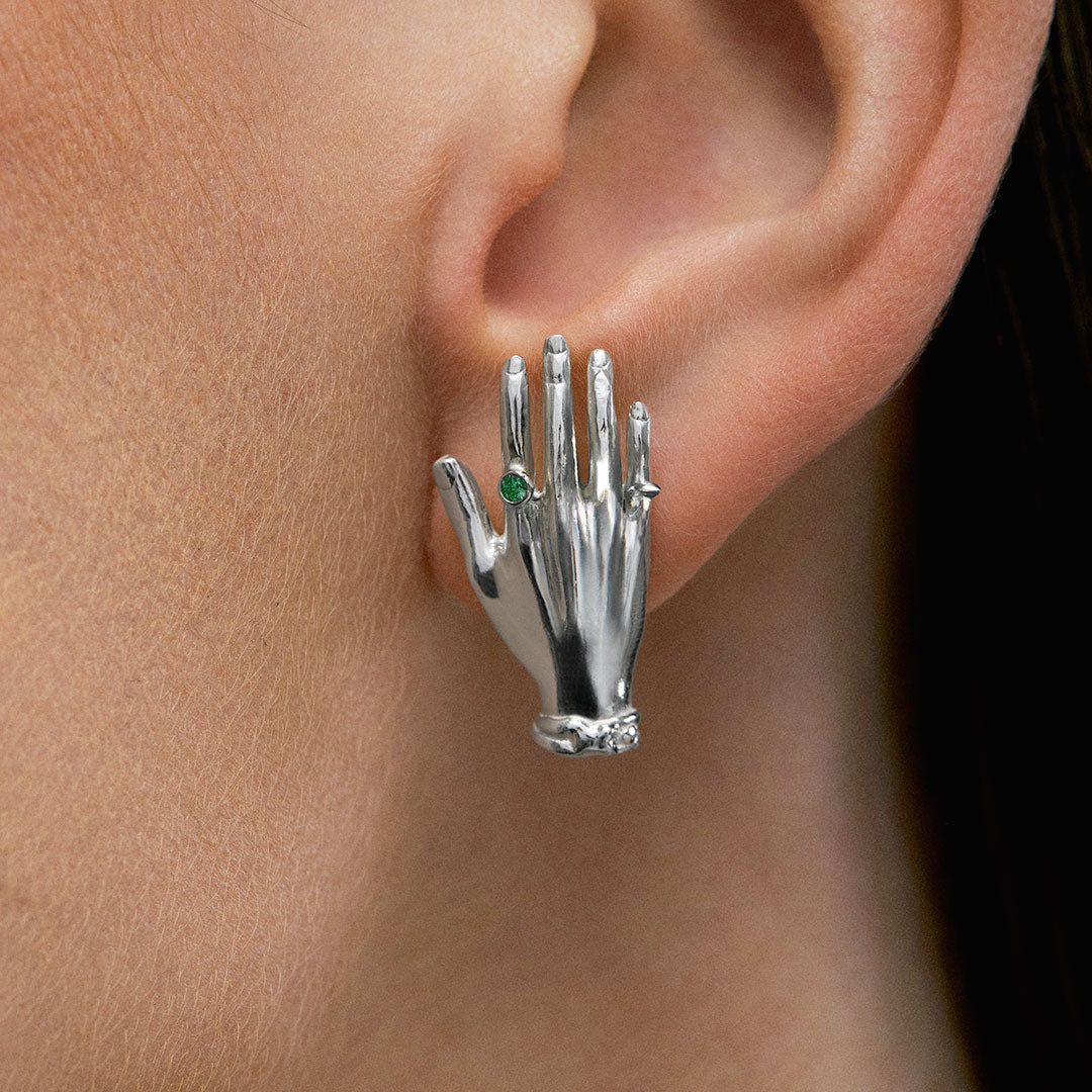 Model wearing hand-shaped earrings in sterling silver and emerald