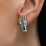 Model wearing hand-shaped earrings in sterling silver and emerald