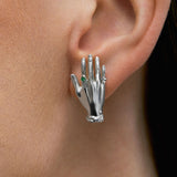 Model wearing hand-shaped earrings in sterling silver and emerald