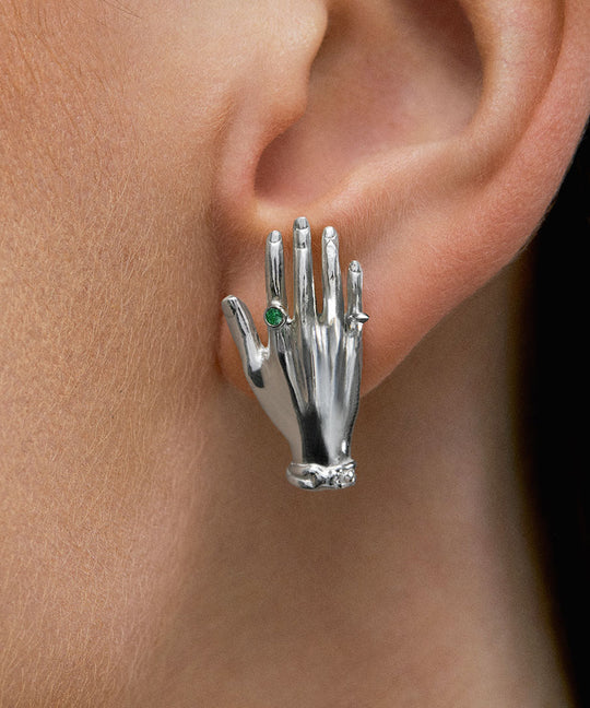 Model wearing hand-shaped earrings in sterling silver and emerald