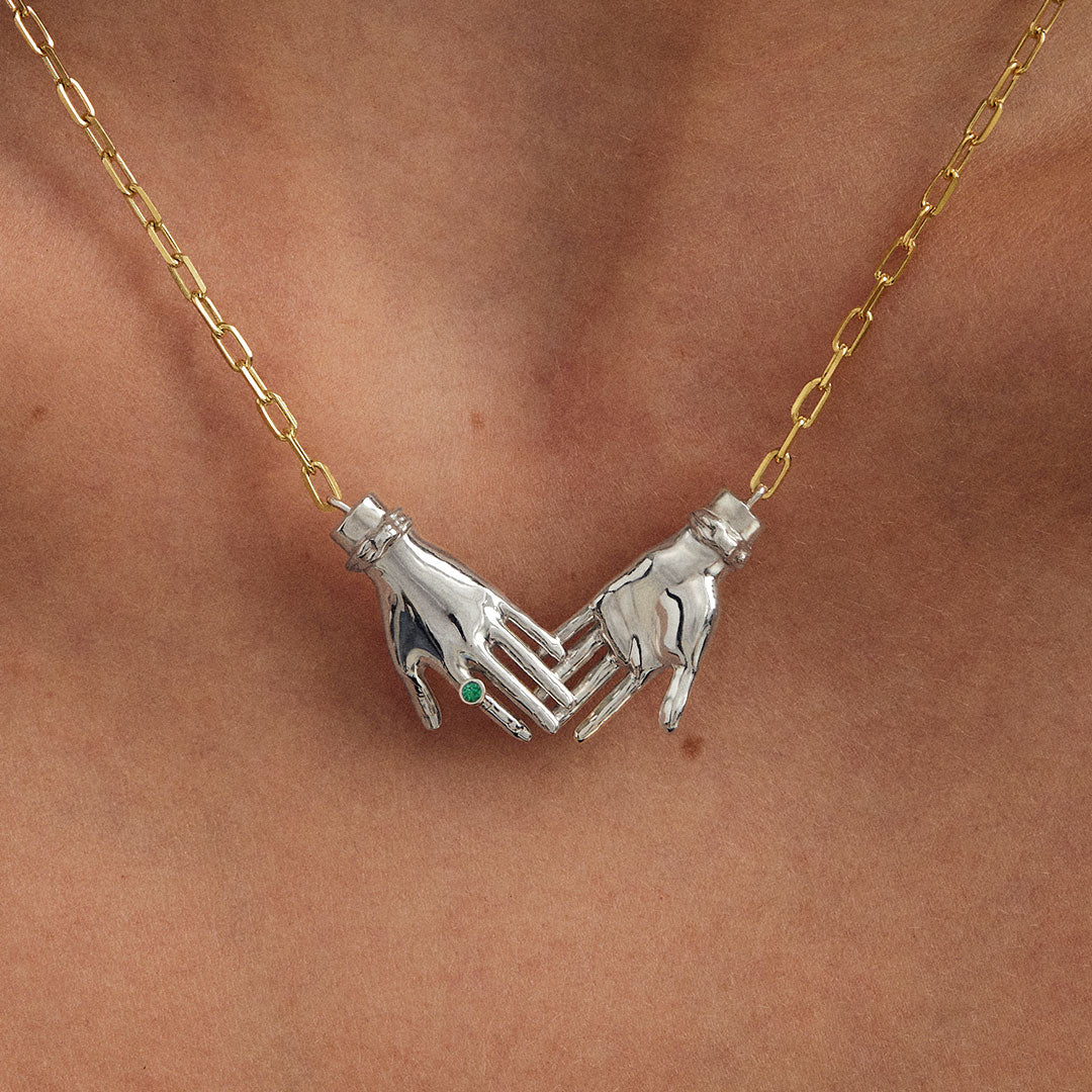 Model wearing sterling silver necklace with 18k gold-plated chain featuring joined hands adorned with emerald