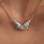 Model wearing sterling silver necklace with 18k gold-plated chain featuring joined hands adorned with emerald