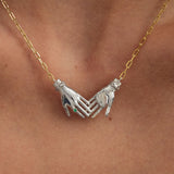 Model wearing sterling silver necklace with 18k gold-plated chain featuring joined hands adorned with emerald