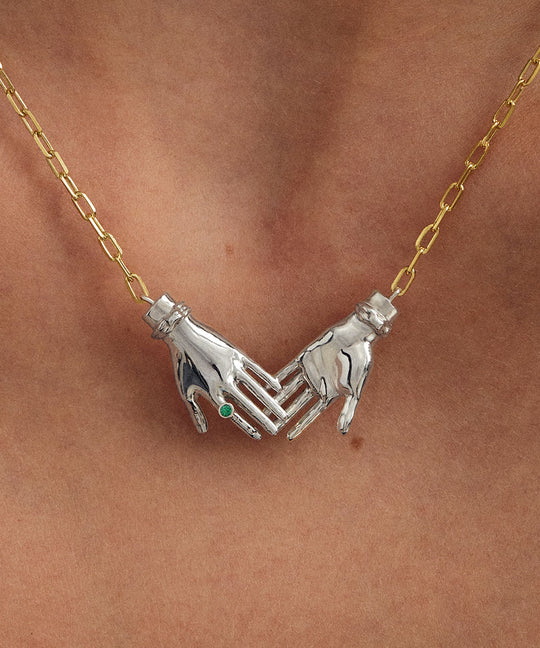 Model wearing sterling silver necklace with 18k gold-plated chain featuring joined hands adorned with emerald
