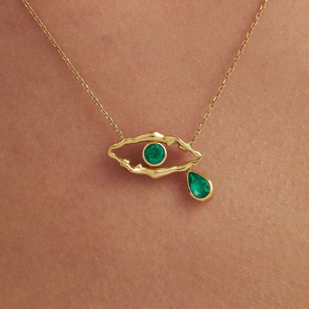 Model wearing 18k gold necklace of female bodies in an eye shape with emeralds