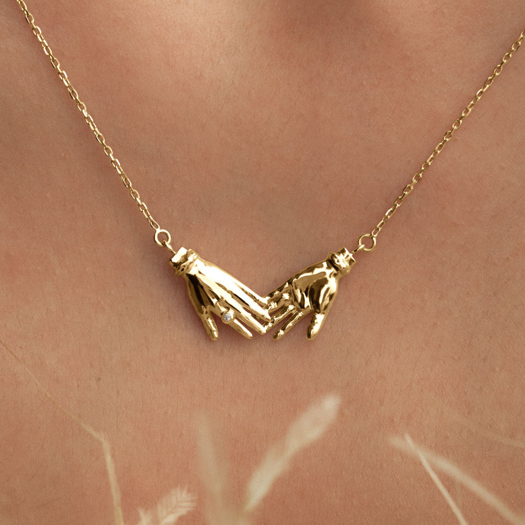 Model wearing 18k gold necklace of hands adorned with diamond