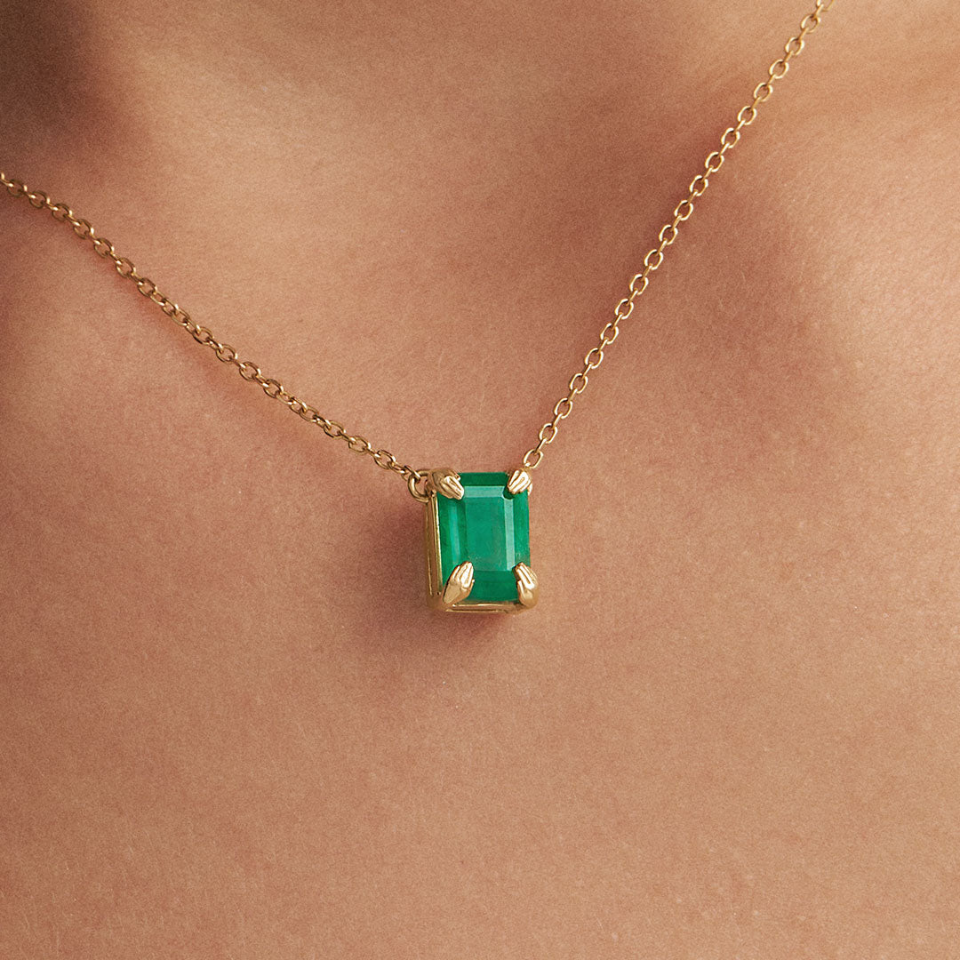 Model wearing 18k gold necklace with sculpted hands and rectangular emerald