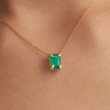 Model wearing 18k gold necklace with sculpted hands and rectangular emerald