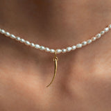Model wearing 18k gold eyelash pendant on a pearl necklace