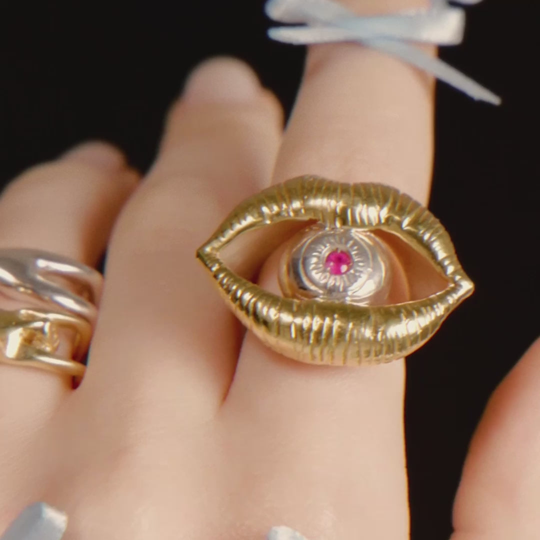 Video of a model wearing a sterling silver ring with 18k gold plating and a ruby, of a mouth with an eye