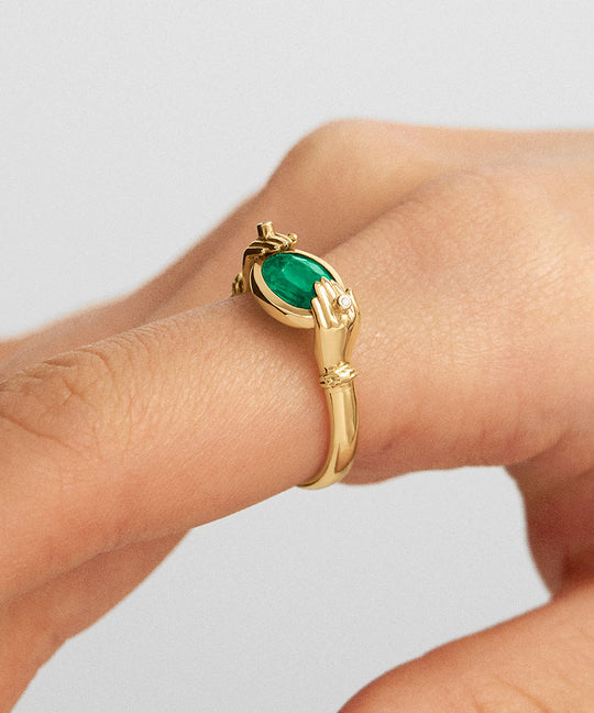 Model wearing 18k gold hands ring adorned with diamonds and an oval emerald