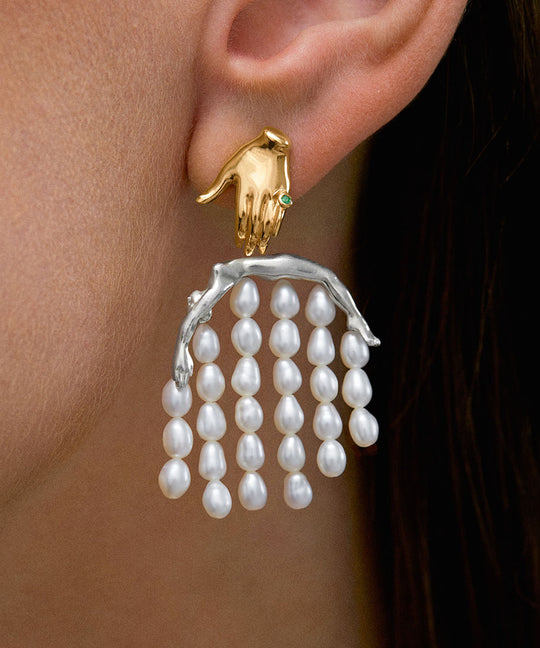 Model wearing 18k gold-plated sterling silver earring featuring a hand and body adorned with pearls and emerald