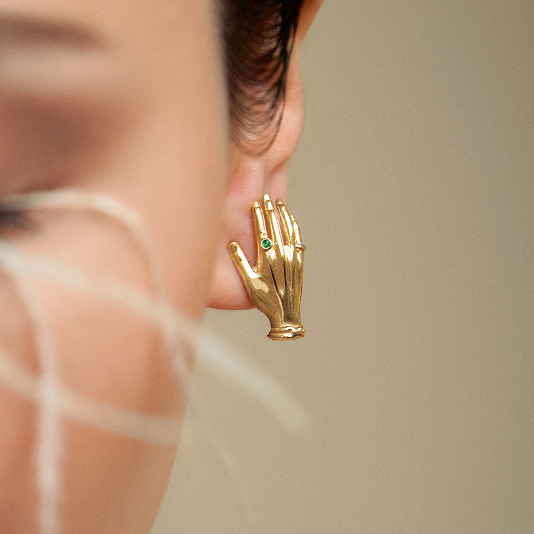 Model wearing hand-shaped earrings in sterling silver with 18k gold plating and emerald