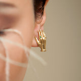 Model wearing hand-shaped earrings in sterling silver with 18k gold plating and emerald