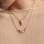 Model wearing necklaces in sterling silver with 18k gold plating featuring hands adorned with emeralds