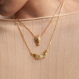 Model wearing necklaces in sterling silver with 18k gold plating featuring hands adorned with emeralds