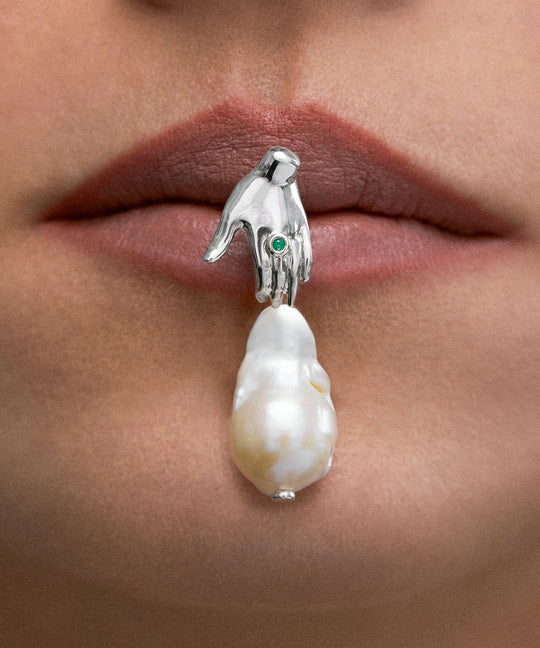 Model wearing hand-shaped earring in sterling silver with emerald and baroque pearl