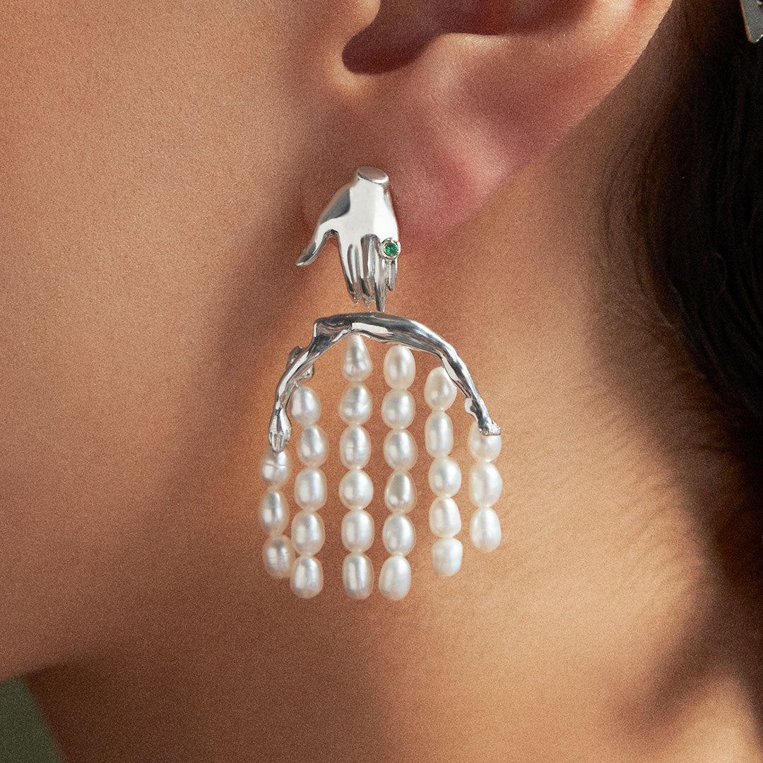 Model wearing sterling silver earring featuring a hand and feminine body adorned with pearls and emerald
