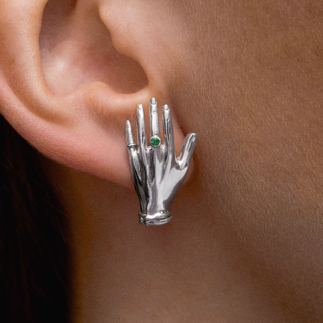 Model wearing hand-shaped earrings in sterling silver adorned with emerald