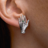 Model wearing hand-shaped earrings in sterling silver adorned with emerald